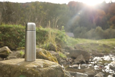 Photo of Metallic thermos on stone near river, space for text