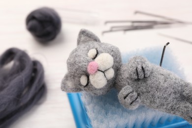 Photo of Felted cat, wool, needles and brush on light table, closeup