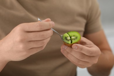 Photo of Man eating kiwi with spoon on blurred background, closeup