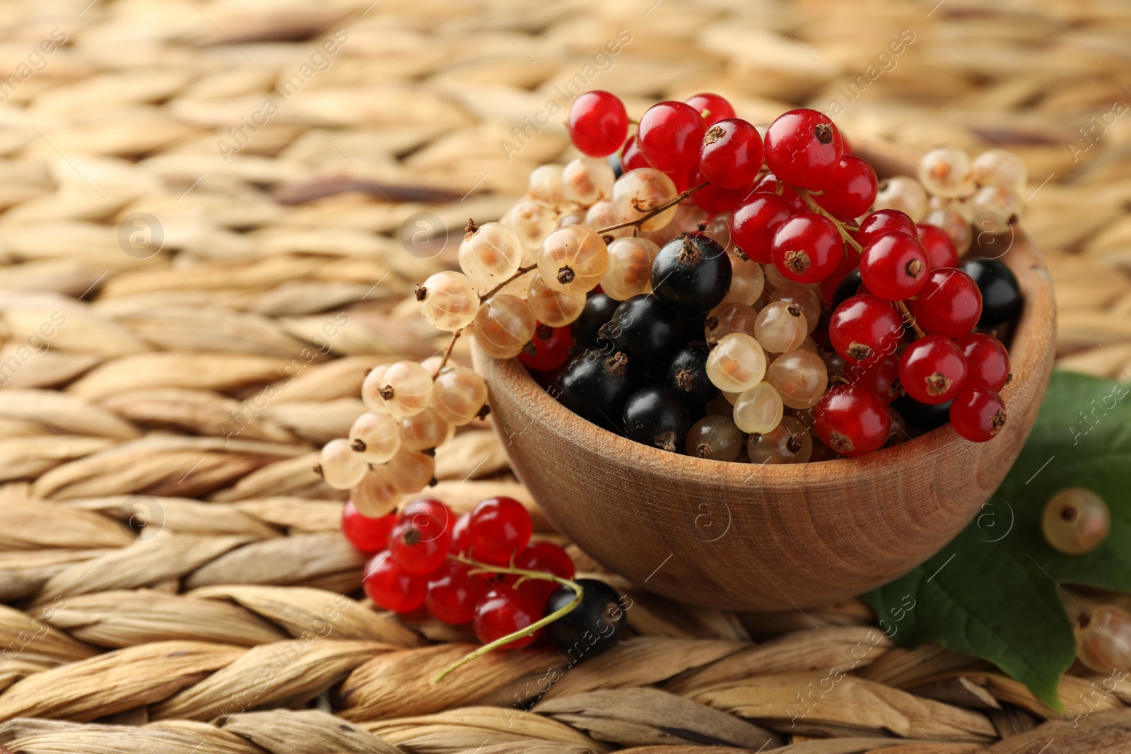 Photo of Different fresh ripe currants and green leaf on wicker surface, closeup. Space for text