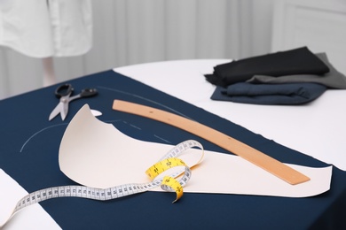 Photo of Ruler, measuring tape, paper template and fabric on table in tailor workshop