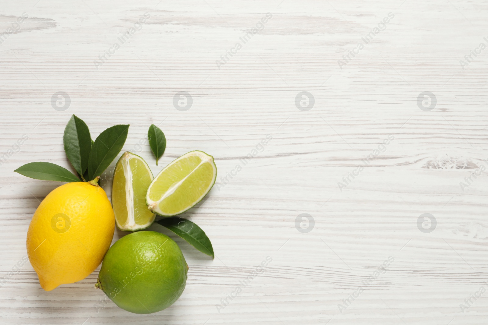 Photo of Fresh ripe lemon, limes and green leaves on white wooden background, flat lay. Space for text