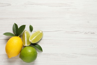 Photo of Fresh ripe lemon, limes and green leaves on white wooden background, flat lay. Space for text