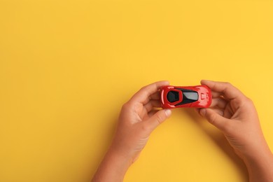 Photo of Child holding toy car on yellow background, top view. Space for text