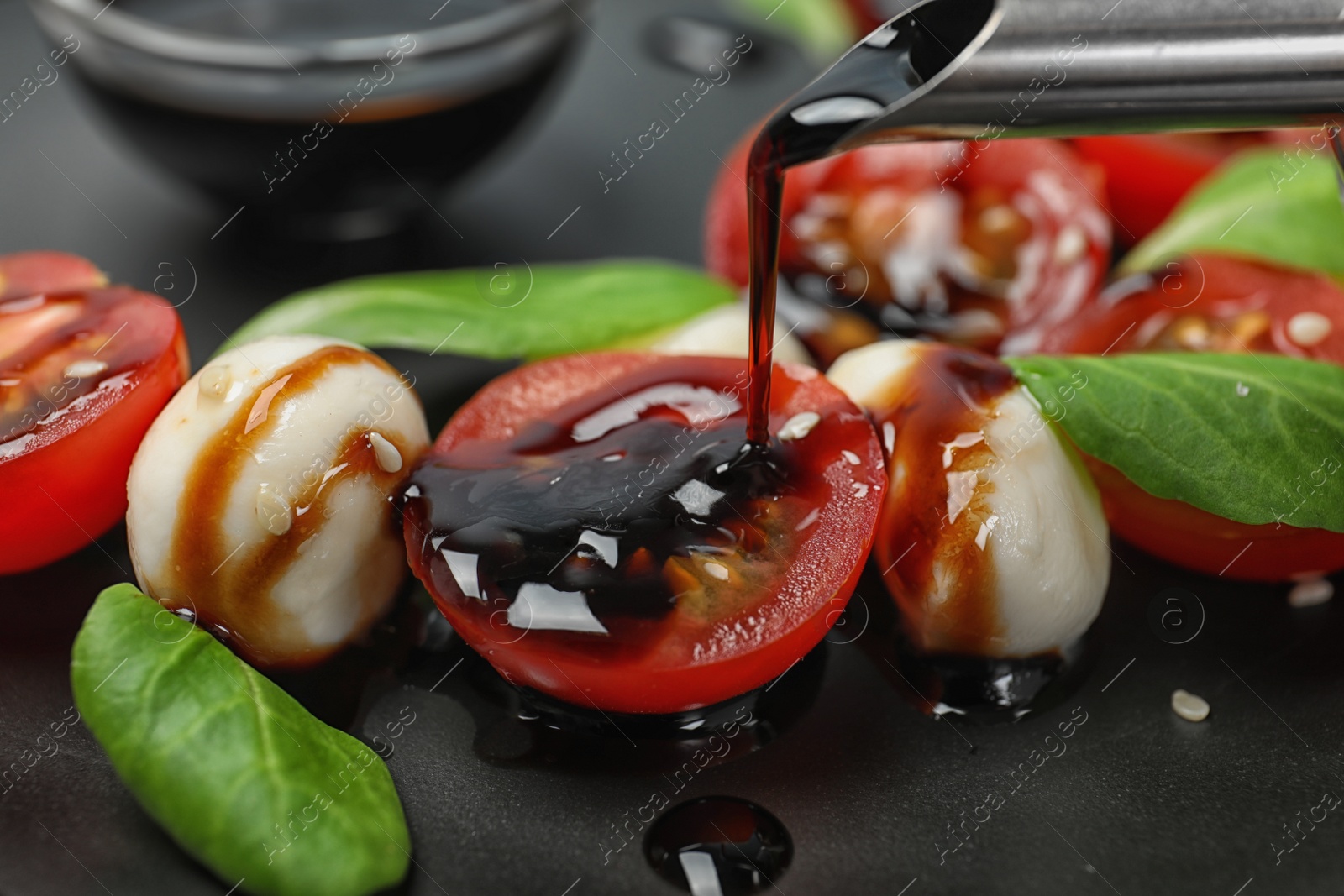 Photo of Pouring balsamic vinegar onto fresh vegetable salad on plate, closeup