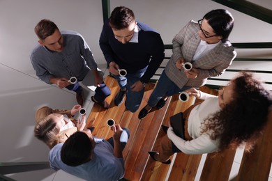 Photo of Group of coworkers talking during coffee break on stairs in office, top view