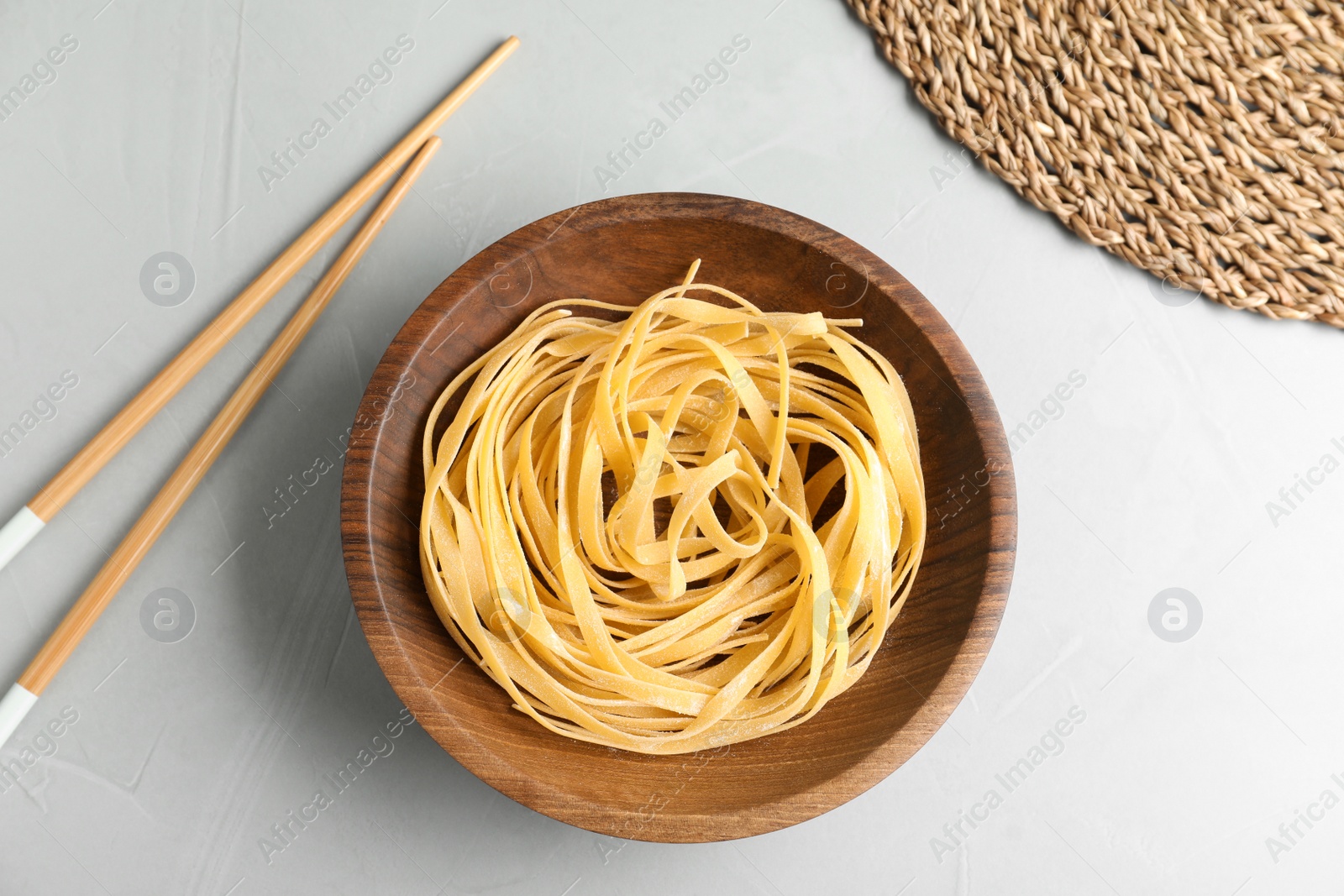 Photo of Plate of uncooked egg noodles and chopsticks on grey table, flat lay