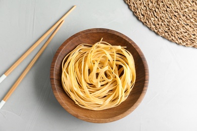 Plate of uncooked egg noodles and chopsticks on grey table, flat lay