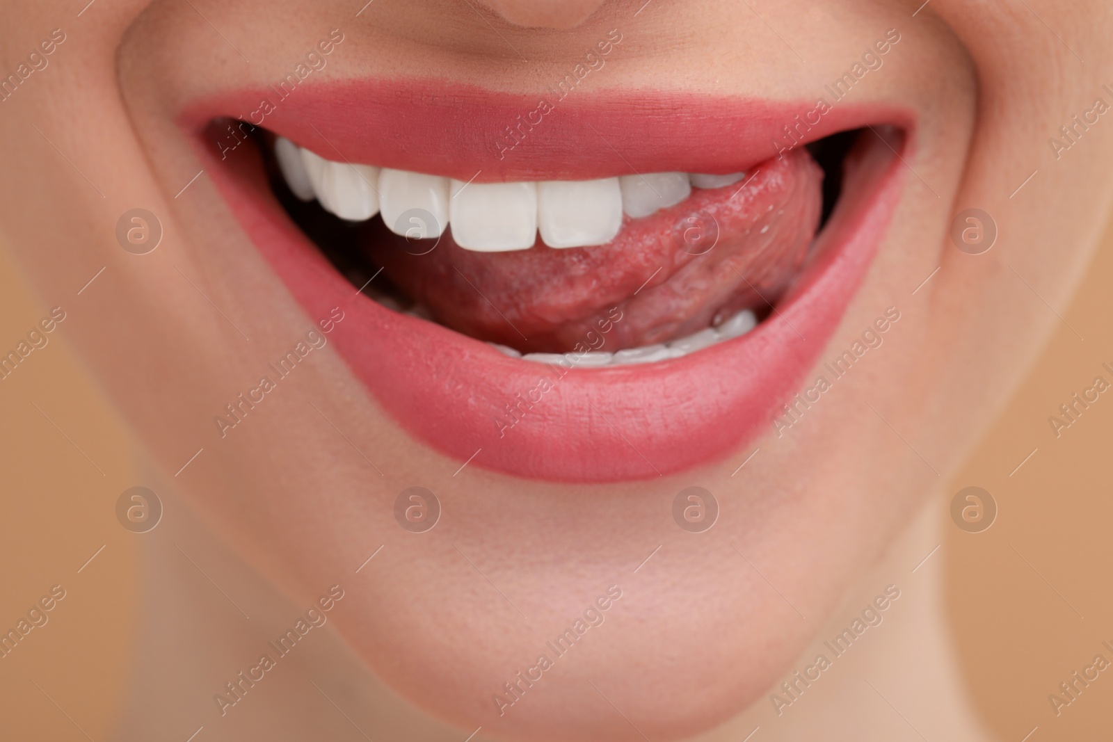 Photo of Young woman licking her teeth on beige background, closeup