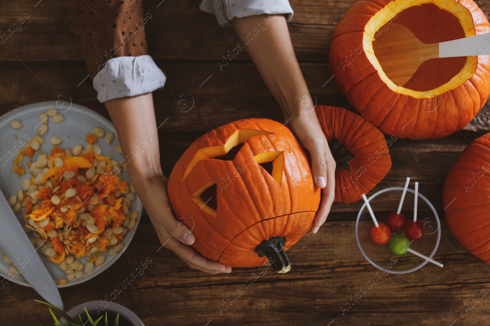 Photo of Woman with pumpkin jack o'lantern at wooden table, top view. Halloween celebration