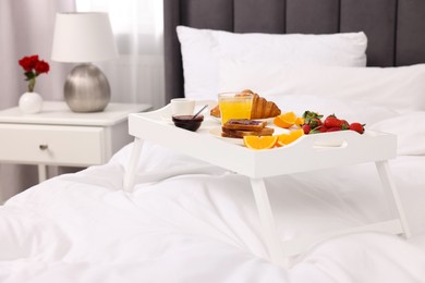 Photo of Tray with delicious breakfast on bed in room, closeup
