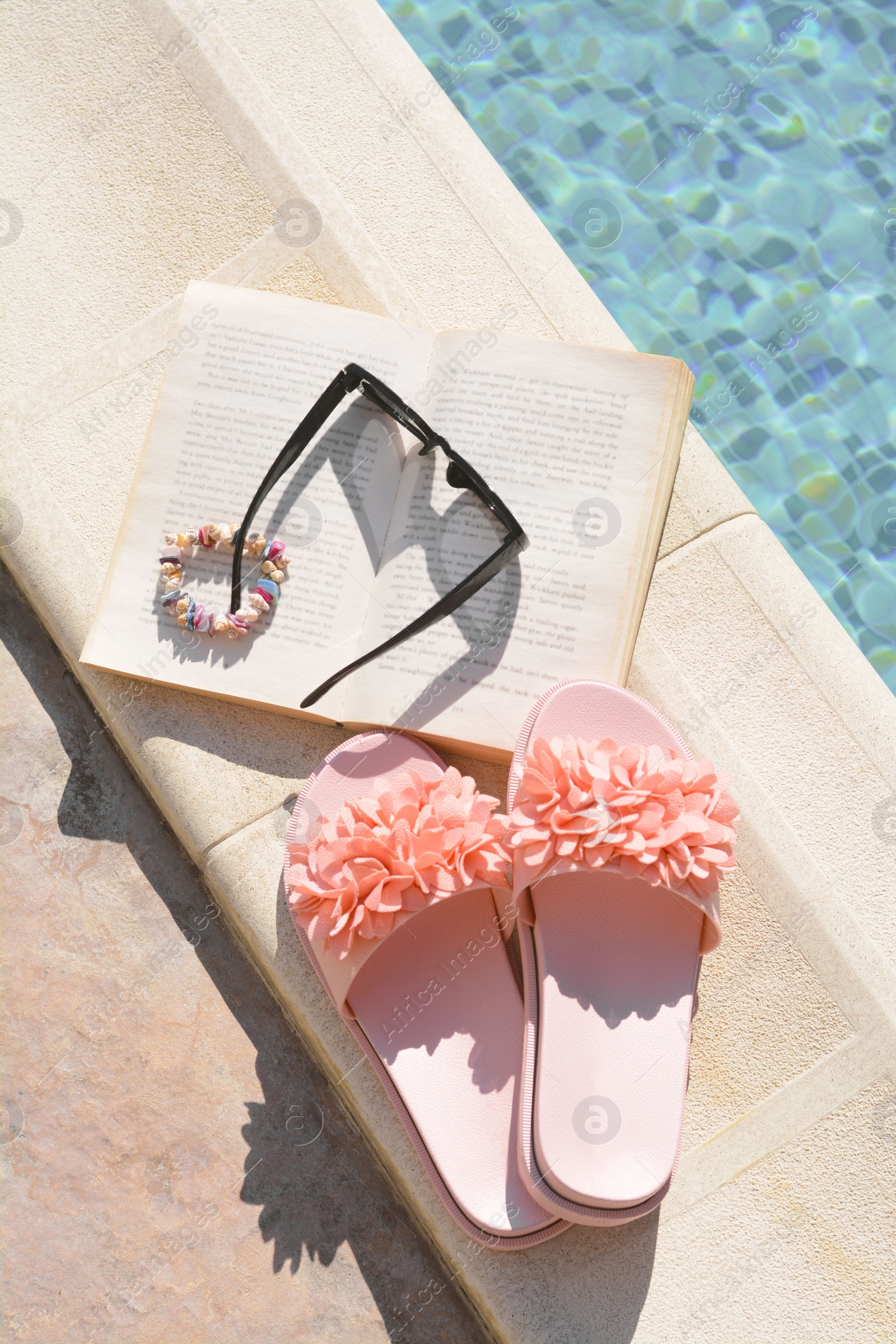 Photo of Book and different beach accessories near outdoor swimming pool on sunny day, flat lay