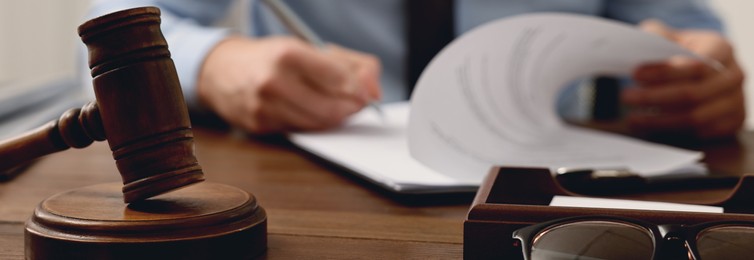 Image of Lawyer working with document at wooden table in office, focus on gavel. Banner design