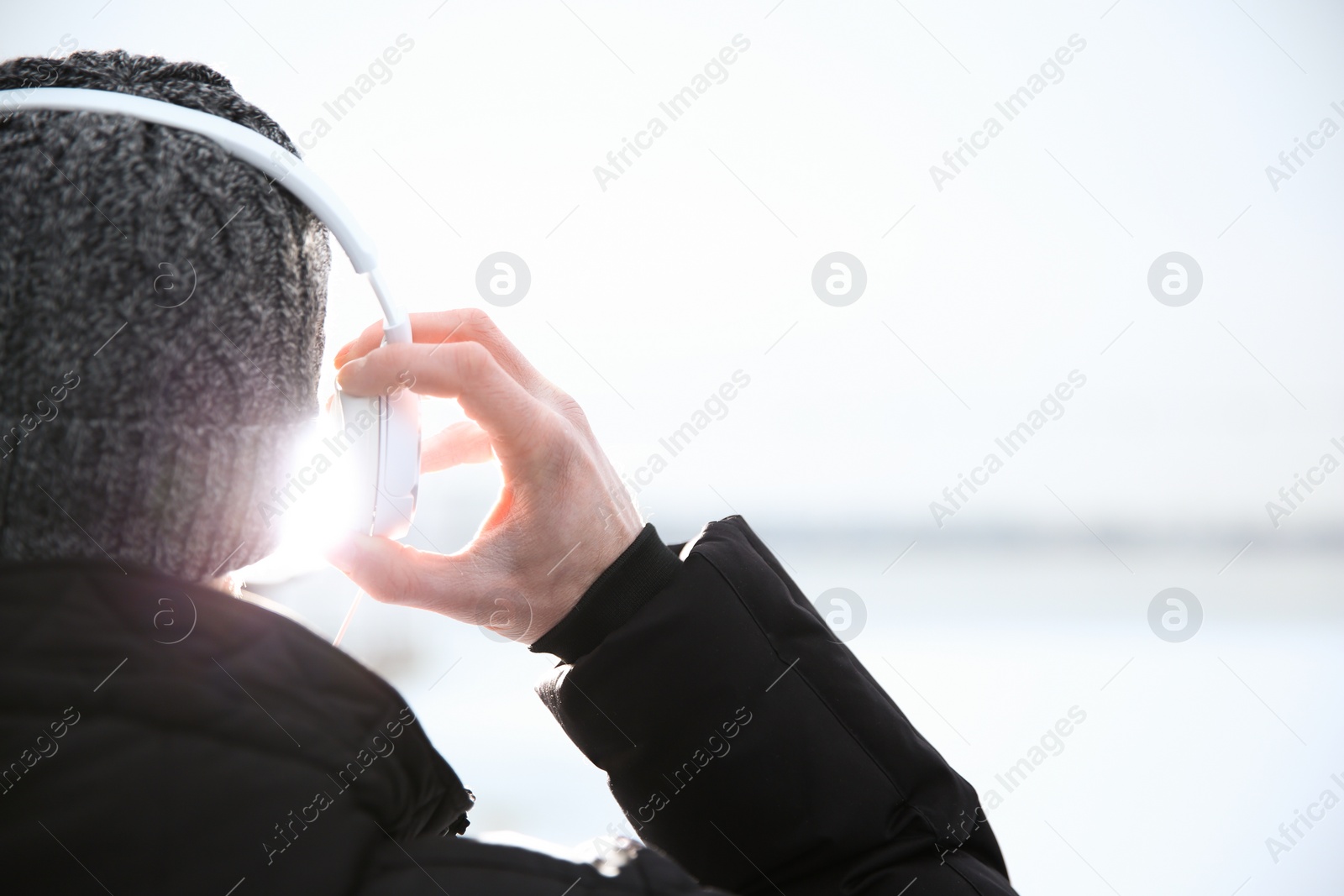 Photo of Young man listening to music with headphones outdoors, closeup. Space for text