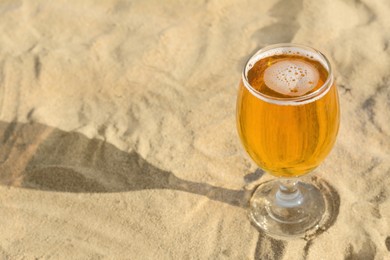 Glass of cold beer on sandy beach. Space for text