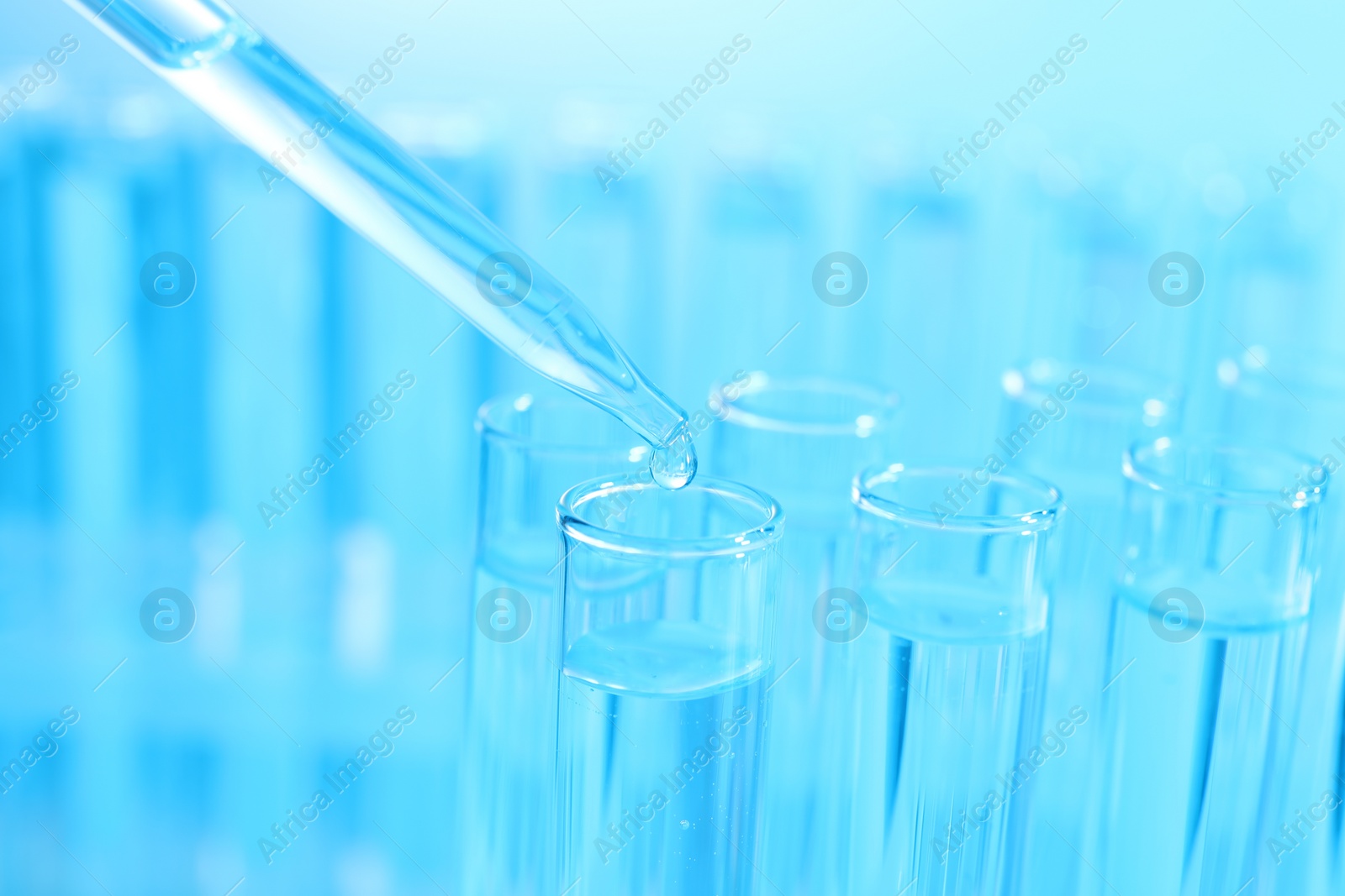 Photo of Dripping liquid from pipette into test tube on light blue background, closeup