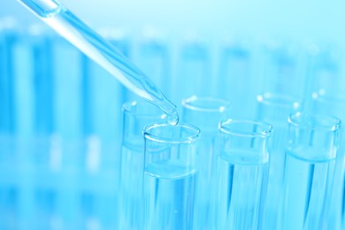 Dripping liquid from pipette into test tube on light blue background, closeup