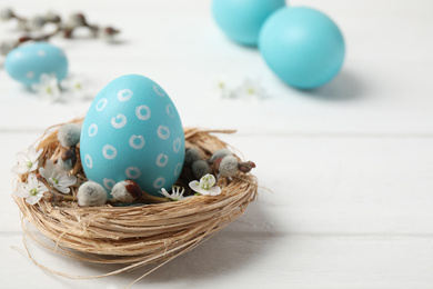 Colorful Easter egg in decorative nest on white wooden table. Space for text