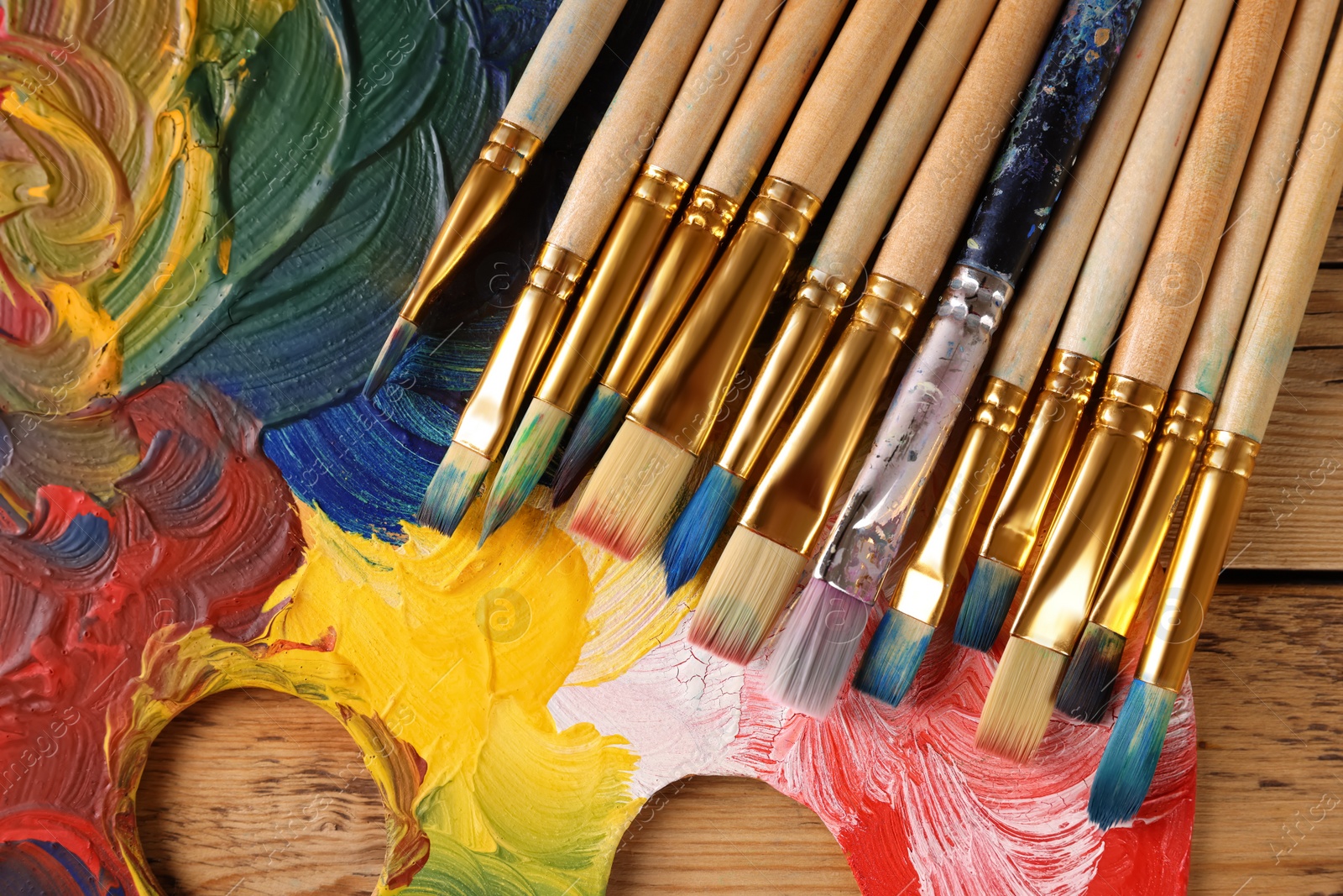 Photo of Many paintbrushes and palette on wooden table, flat lay