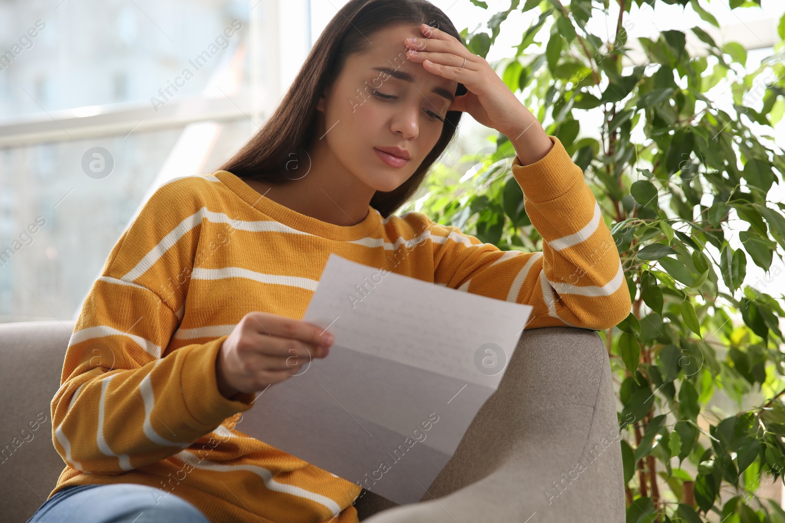 Photo of Worried woman reading letter on sofa at home