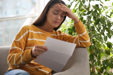 Worried woman reading letter on sofa at home