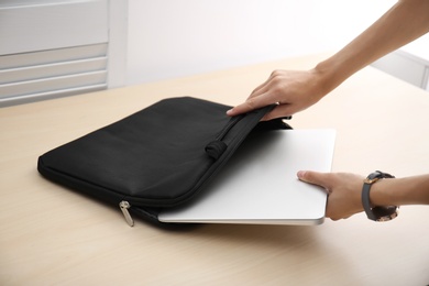 Photo of Woman putting laptop into case at table, closeup