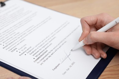 Woman signing contract at wooden table, closeup.