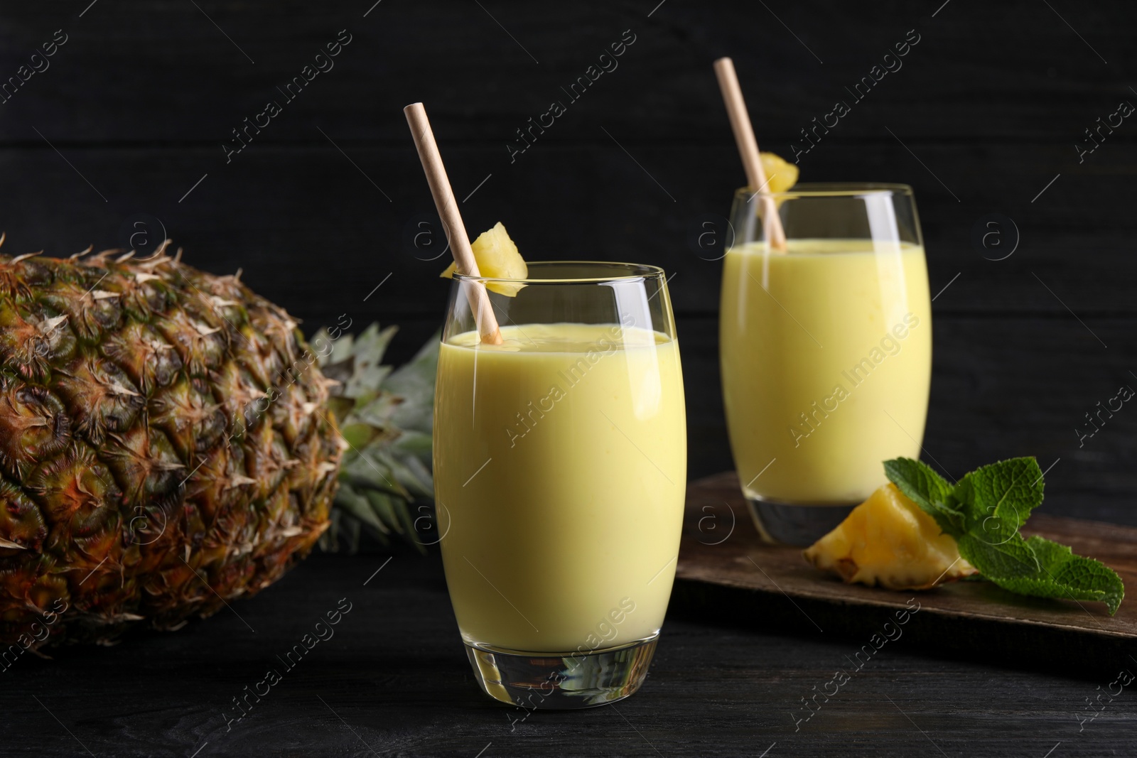 Tasty pineapple smoothie and fruit on black table Photo of Tasty pineapple smoothie and fruit on black table