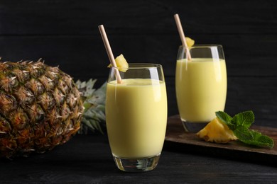 Photo of Tasty pineapple smoothie and fruit on black table