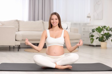 Pregnant woman meditating on yoga mat at home