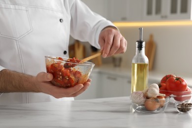 Photo of Professional chef making delicious tomato sauce at white marble table indoors, closeup