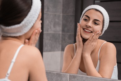 Photo of Young woman with headband washing her face near mirror in bathroom