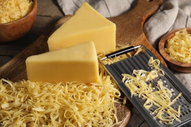 Grated, whole pieces of cheese and grater on table, closeup