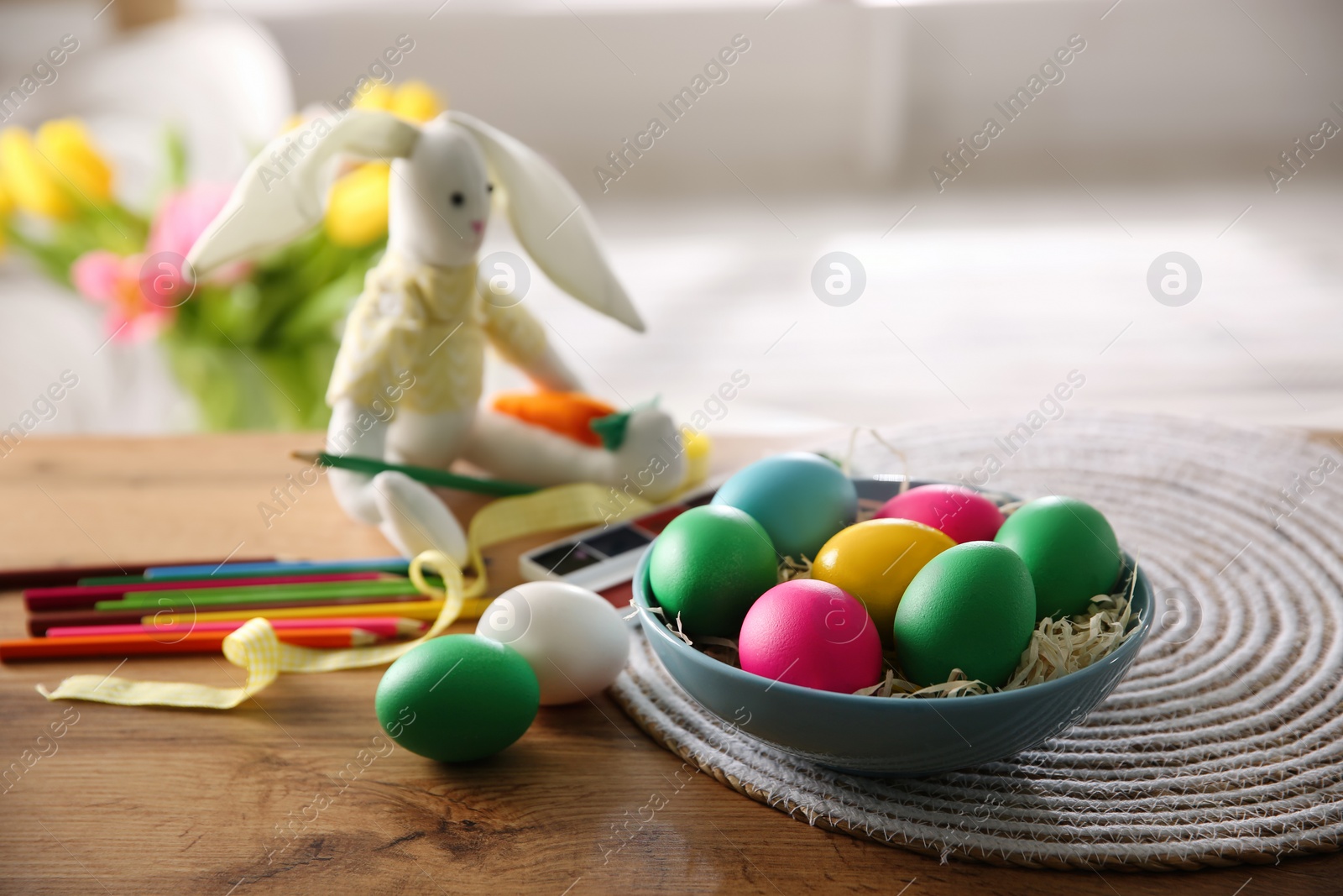 Photo of Bright painted Easter eggs, color pencils and toy bunny on wooden table indoors