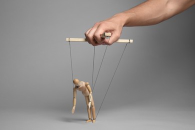 Photo of Man pulling strings of puppet on gray background, closeup