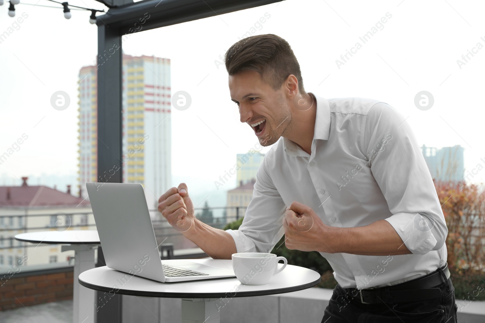 Photo of Emotional businessman working with laptop in outdoor cafe. Corporate blog