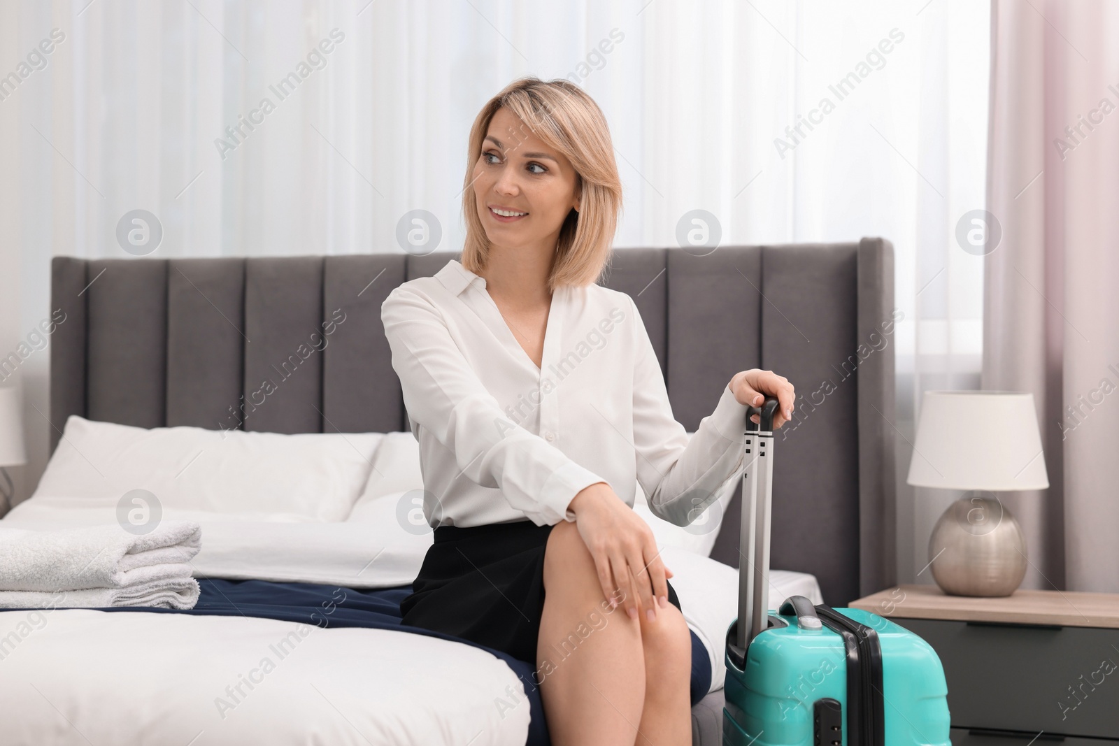 Photo of Smiling businesswoman relaxing on bed in stylish hotel room