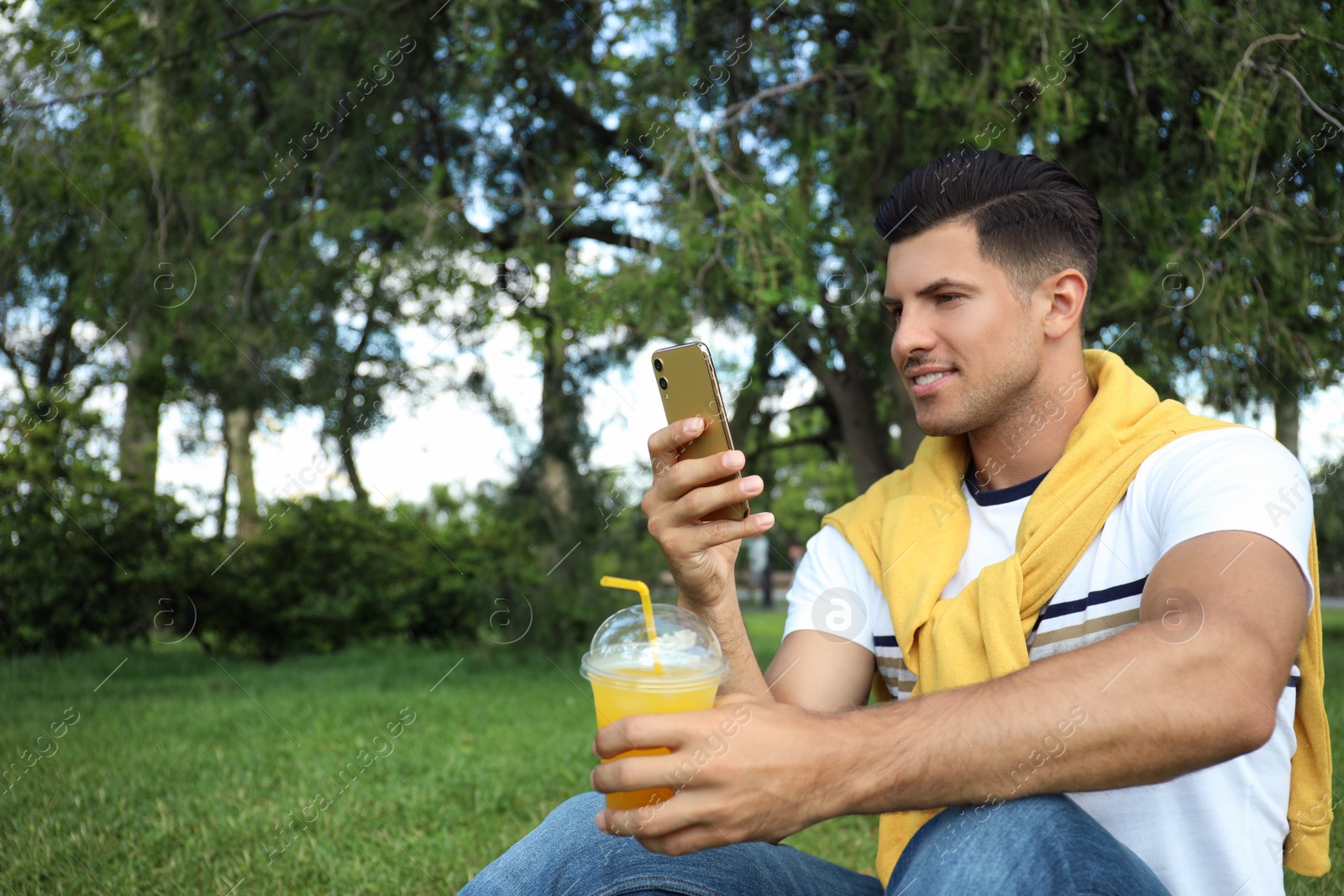 Photo of Handsome man with smartphone and refreshing drink in park