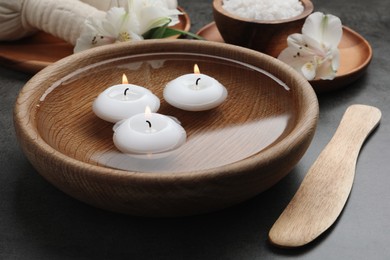 Spa composition with burning candles in bowl with water on grey table