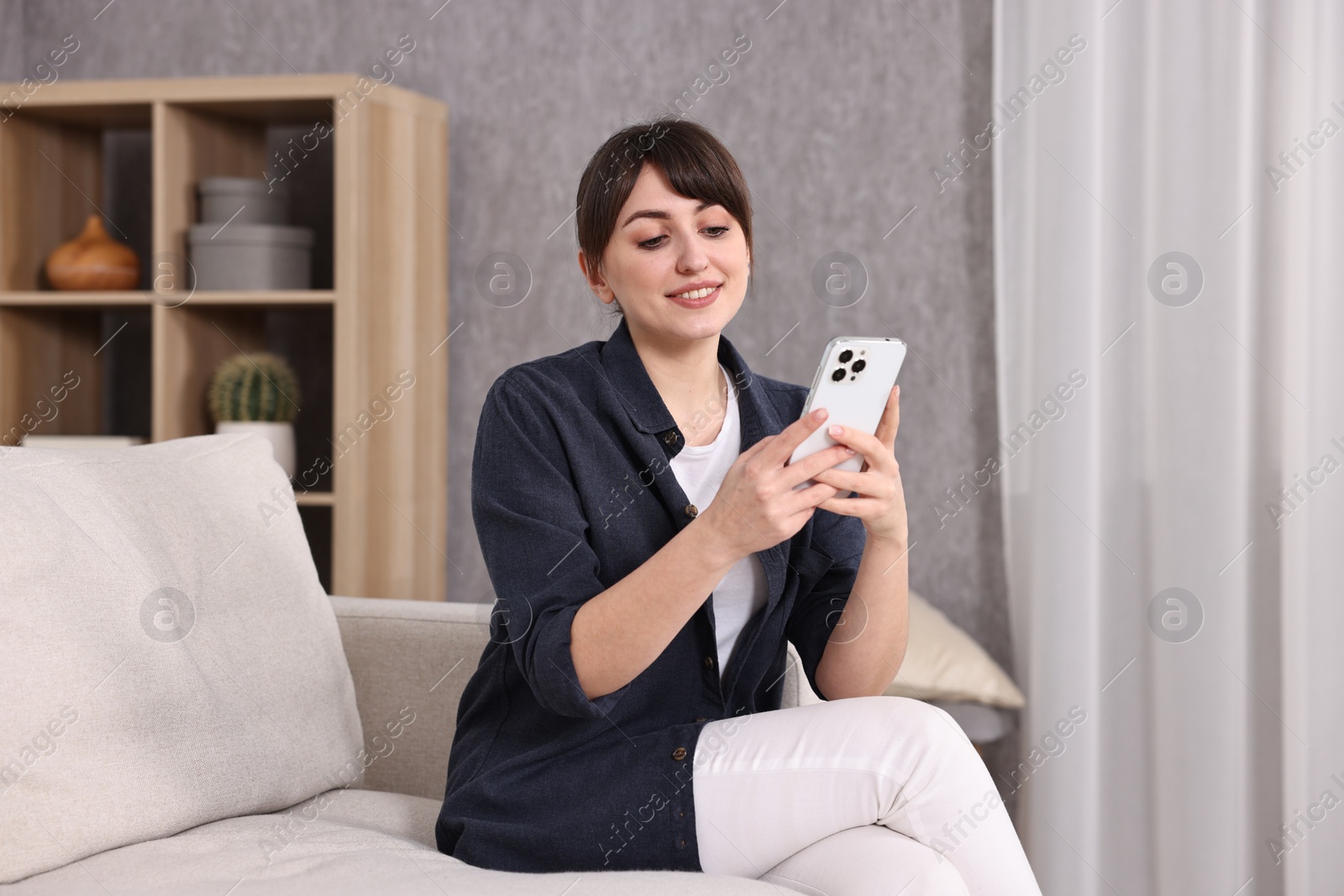 Photo of Beautiful young housewife using smartphone on sofa at home