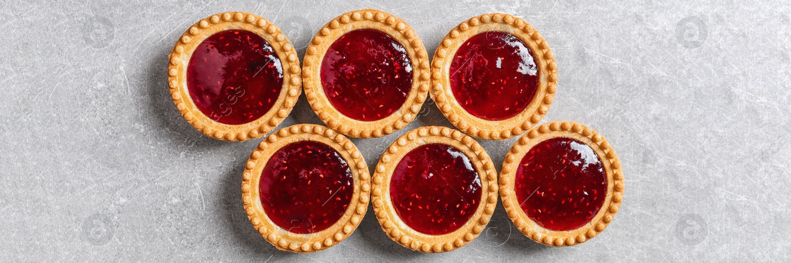 Image of Tasty tartlets with jam on light grey table, flat lay. Banner design