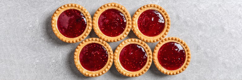 Tasty tartlets with jam on light grey table, flat lay. Banner design