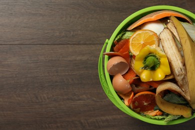 Natural garbage in trash bin on wooden background, top view with space for text. Composting of organic waste