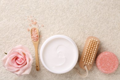 Flat lay composition with moisturizing cream in open jar and other body care products on light textured table