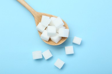 Photo of White sugar cubes and wooden spoon on light blue background, top view