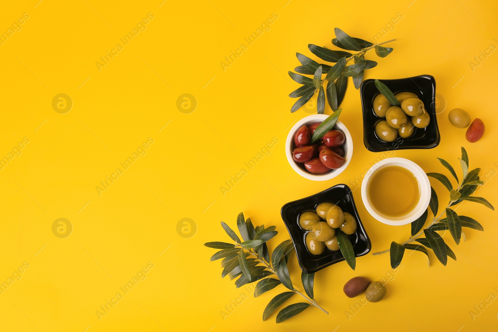 Photo of Bowl of oil, olives and tree twigs on yellow background, flat lay. Space for text