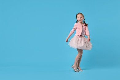 Photo of Cute little girl dancing on light blue background, space for text