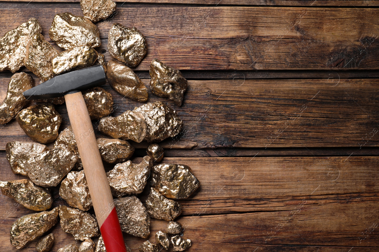 Photo of Pile of gold nuggets and hammer on wooden table, flat lay. Space for text