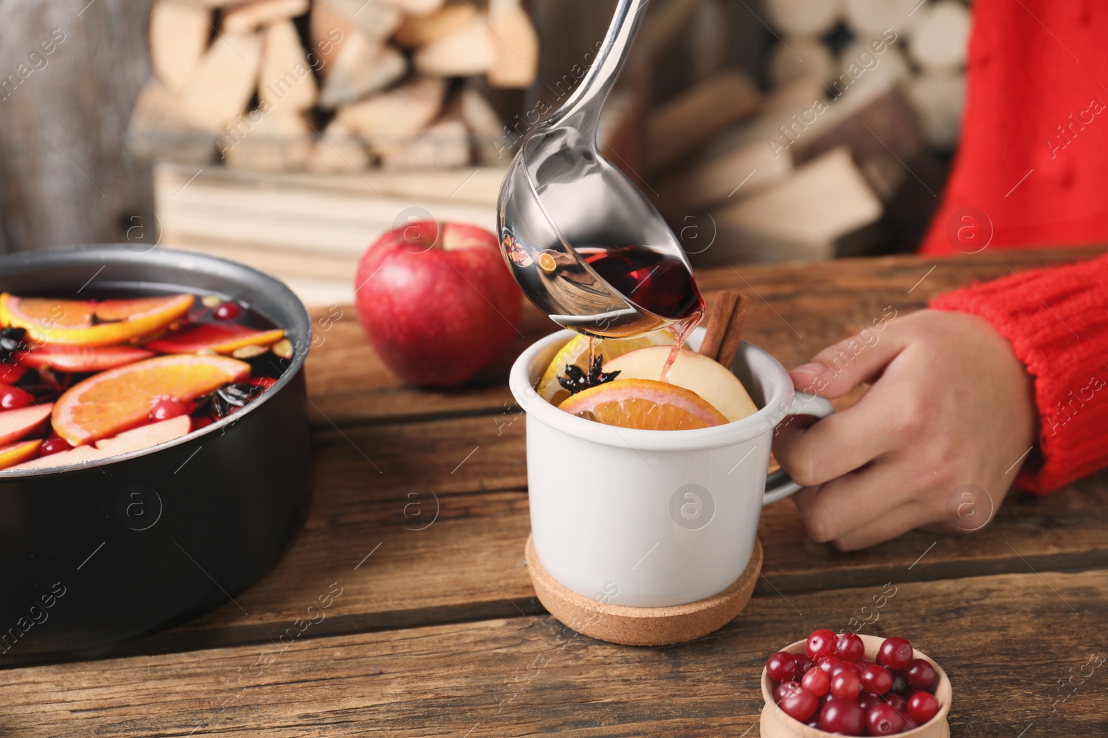 Photo of Woman pouring hot mulled wine into cup at wooden table, closeup