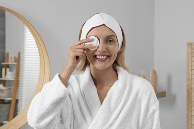 Photo of Young woman cleaning her face with cotton pad near in bathroom